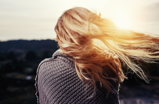 Blonde woman wrapped in a cardigan watching the sunset