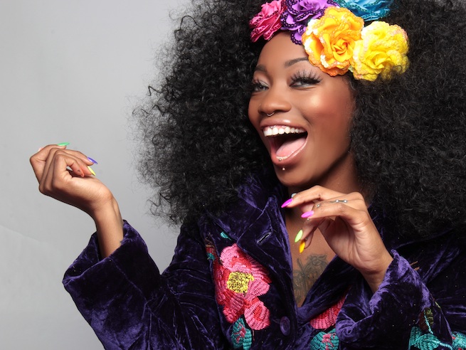 woman with black curly hair and bright coloured nails and accessories