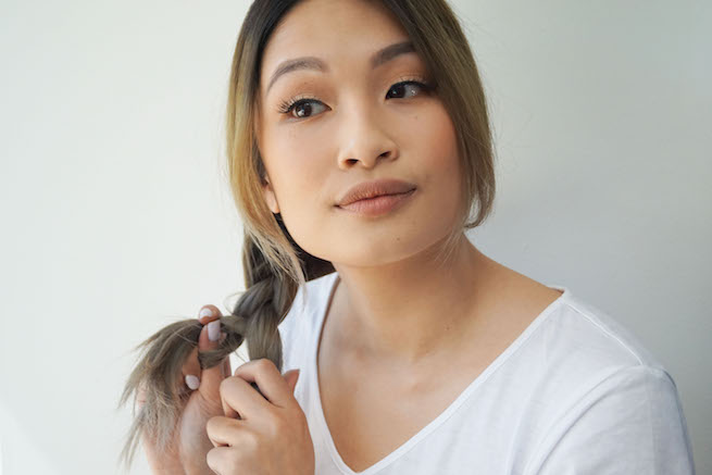 woman tying up ponytail for side swept braid hairstyle