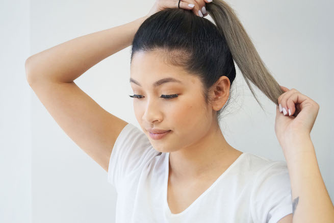Woman tying up pony tail demonstrating the sleek pony tail hairstyle