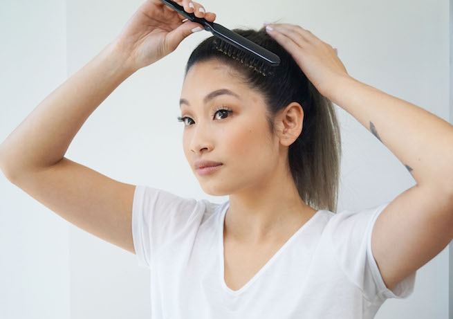 Woman brushing out stray hairs for the sleek ponytail hairstyle